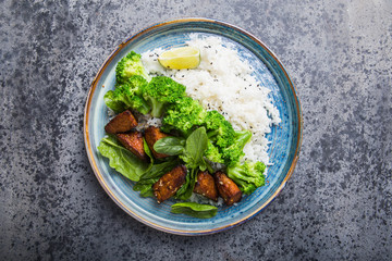 Vegan teryaki  tempeh or tempe buddha bowl  with rice, steamed broccoli, spinach  and lime on gray   background. Healthy food