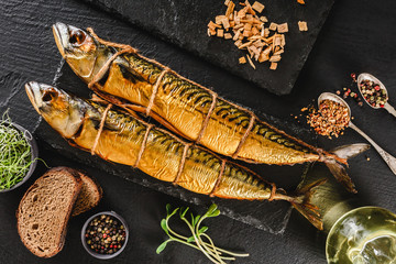 Appetizing smoked fishes with sawdust and burlap texture on slate stone background. Mediterranean food, herring fish, seafood, top view