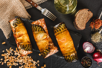 Fototapeta na wymiar Appetizing smoked mackerel fish rolls with spices, pepper and bread on dark slate background. Mediterranean food, herring fish, seafood, top view