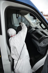 Worker in protective suit disinfects the car