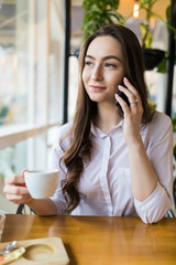 Carefree talk with friend. Cheerful young woman talking on phone and smiling while enjoying coffee in cafe