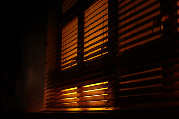 Dark, moody atmosphere set by yellow light softly piercing through the blinds. The shutters create...