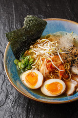 Asian noodle soup, ramen with pork, tofu, kimchi, vegetables and egg in blue bowl. Slate background. Top view. Bowl of asian style soup. Japanese cuisine. Top view. Banner. Asian food