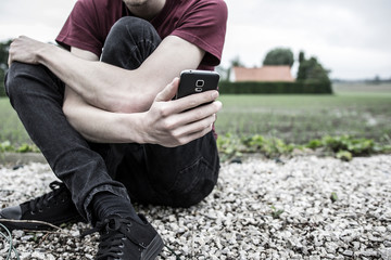 An anonymous young man or boy holding his phone and looking at it. A concept about struggling with yourself, being mentally and physically tangled up, autism, online bullying and suicide thoughts.