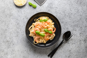 Italian pasta fettuccine with shrimps in black bowl on grey table. Top view.