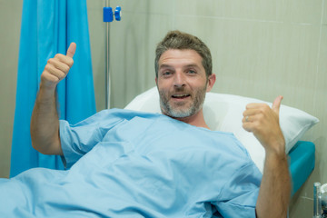 positive and hopeful hospital patient smiling before adversity - young attractive and trustful man lying on clinic bed responding to treatment and healing