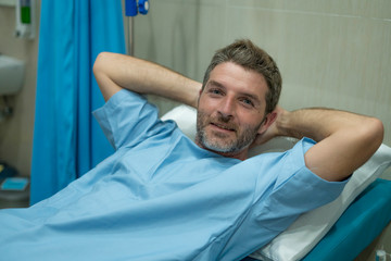 positive and hopeful hospital patient smiling before adversity - young attractive and trustful man lying on clinic bed responding to treatment and healing