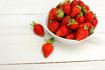 Fresh ripe delicious strawberries in a white bowl on a wooden background