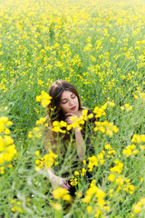 Fototapeta premium Girl in dark clothes with beautiful hair sitting in a field of yellow rape. Warm spring day