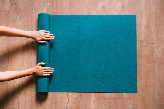 Fit woman folding blue exercise mat on wooden floor before or after working out in yoga studio or at home. Equipment for fitness, pilates or yoga, well being concept. Flat lay, space for text.