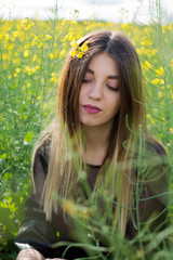 Girl in dark clothes with beautiful hair sitting in a field of yellow rape. Warm spring day