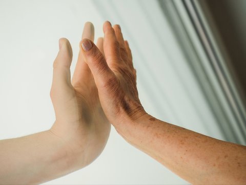 Close Up Of Hands Of Elderly And Young Women On Window