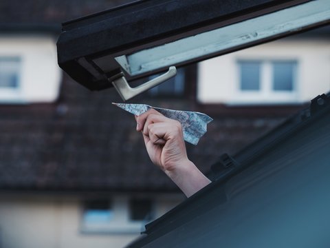 Hand holding paper plane out of skylight window