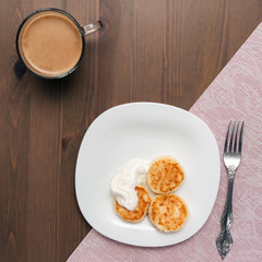 syrniki on a wooden brown table with a pink napkin and coffee