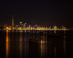 Fototapeta na wymiar Bright lights of Auckland city downtown and the port reflected in Okahu bay with a small boat in the foreground. Soft focus