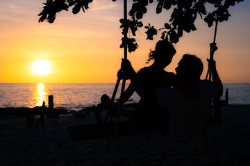 Couple on a swing at sunset in the beach. Silhouette.