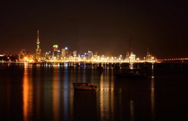 Fototapeta na wymiar Midnight in Auckland. The lights of city downtown and the port reflected in Okahu bay with a small boat in the foreground. Soft focus