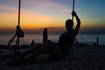 Young woman at dusk sitting on a swing.
