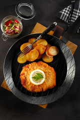 Typical Austrian viennese Schnitzel - wiener schnitzel - with potatoes in iron pan on black background -escalope-