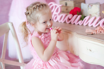 Fototapeta premium Little girl in a pink dress paints lips