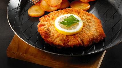 Typical Austrian viennese Schnitzel - wiener schnitzel - with potatoes in iron pan on black...