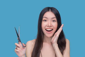 Obraz premium Young asian woman holding scissors and looking excited