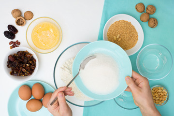 ingredients for the recipe homemade oatmeal cookies with dates, peanuts, coconut chips in glass plates on a light background. the view from the top, mixing with your hands ingredients