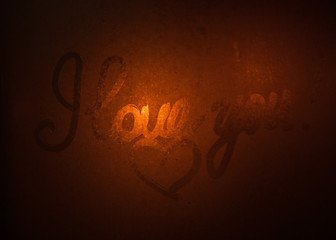 Night rain drops on a glass window with blurred red sky background, view through a wet and sweaty window with heart sign. I love you inscription.