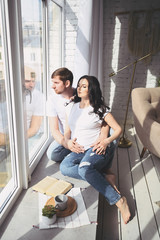 Pregnancy and people concept - happy man hugging his beautiful pregnant wife at home. Future parents waiting unborn baby. Love, relationship, birth, happy family concept - young lovely married couple