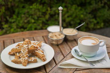 a plate of homemade biscotti cookies and a Cup of coffee with cream and sugar on the wooden table. Blurred background
