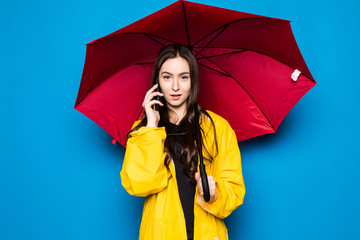 Happy pretty smiling young woman with umbrella talk smartphone in autumn day over colorful blue background