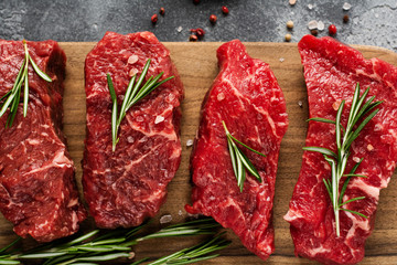 Raw beef steak with spices, onions and rosemary on dark slate or concrete background. Top view
