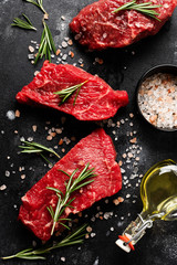 Raw beef steak with spices, onions and rosemary on dark slate or concrete background. Top view