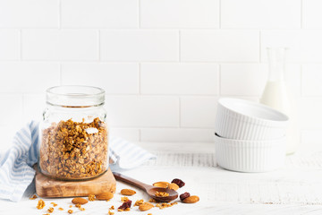 Oat granola with a bottle of milk, nuts and dried fruits, ceramic bowls for preparing a healthy breakfast on a bright kitchen table. Scandinavian white style. Selective focus.