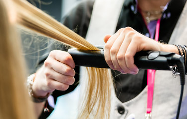 Fototapeta na wymiar Professional hairdresser straightening long blond hair using straightener