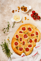 Italian traditional focaccia bread baking with with cherry tomatoes, parmesan and rosemary on light brown background. Top view.