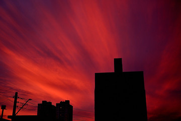 Céu laranja com nuvens no final da tarde e silueta de prédios na cidade