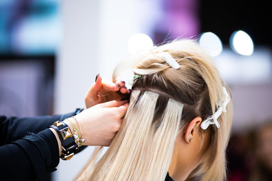Professional hairdresser making hair extensions for blonde girl in a beauty salon