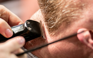 Fototapeta premium Professional barber cutting client beard to perfect shape using trimmer, close up view