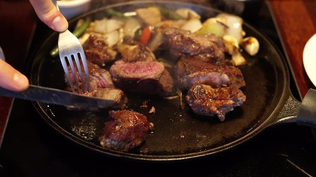 Close-up - man hands cutting middle ready beef steak on frying pan into pieces
