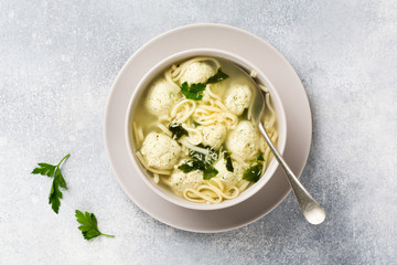 Soup with chicken meatballs and egg paste, Parmesan cheese, parsley in a ceramic bowl on a gray table background. Traditional Italian broth.  Top view.