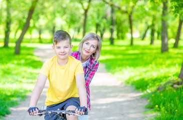 Happy family. Sporty family leisure. Mom teaches her young son ride a bike in summer park. Empty space for text