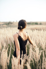 Brunette girl in a black dress on the field in summer sunny day