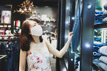 Asian woman wearing face mask choosing jeans in mall.