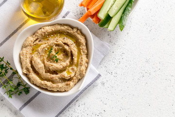 hummus sauce in a bowl, sesame seeds, olive oil, cucumber and carrots on a light background