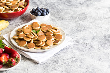 Tiny pancakes for breakfast. Cereal pancakes with blueberries, bananas, strawberries on grey background. Trendy food. Copy space for text or design
