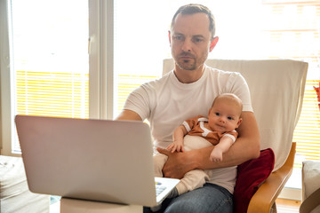 Young man parent working on laptop computer at home and take care of baby