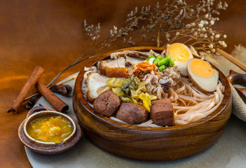 Traditional chinese Sliced stewed pork noodles with Pork bone broth and boiled egg, tofu in wooden bowl Served with pickled chillies. Asian style food, Selective focus.