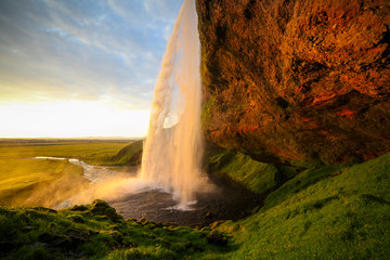 Fototapeta na wymiar Waterfall Selandjafoss Iceland at sunset or sunrise. Beautiful waterfall in Iceland. Golden hour. Cave and waterfall. Travel in Iceland. Beautiful sky against the big waterfall. inside the water. 