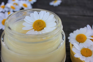 Natural chamomile face cream and fresh daisy flowers on dark rustic wooden background. Homemade...